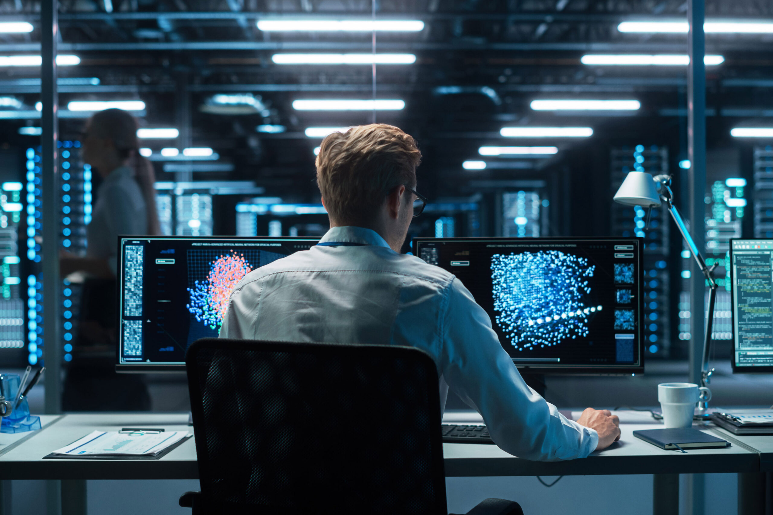 In the Futuristic Laboratory or Office Male Scientists Working at the Two Monitors. Developer Writing Code at the Evening. Computer Engineer Create Neural Network at His Workstation